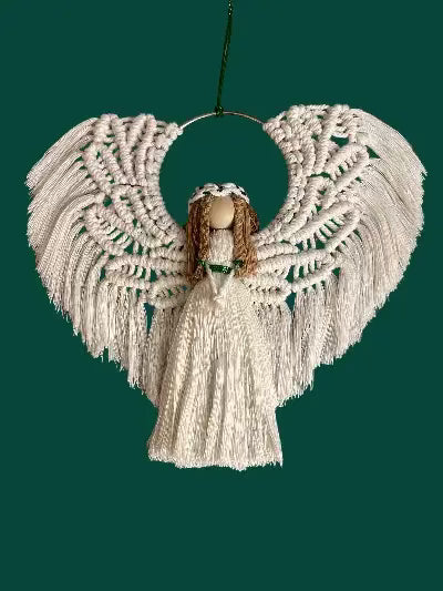handmade macrame angel ornamnt with braided hairm white cotton wings, a  white-and-green halo, and a flowing dress, displayed on a green textured background.
